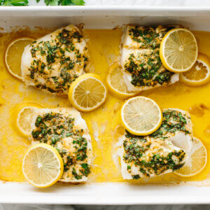 Baked cod in a baking pan topped with lemon slices.