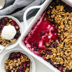 A baking pan of berry crisp and two servings in bowls.