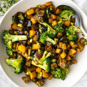 A bowl of eggplant and butternut squash stir fry next to a napkin