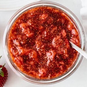 Chia seed jam in a container next to fresh strawberries.