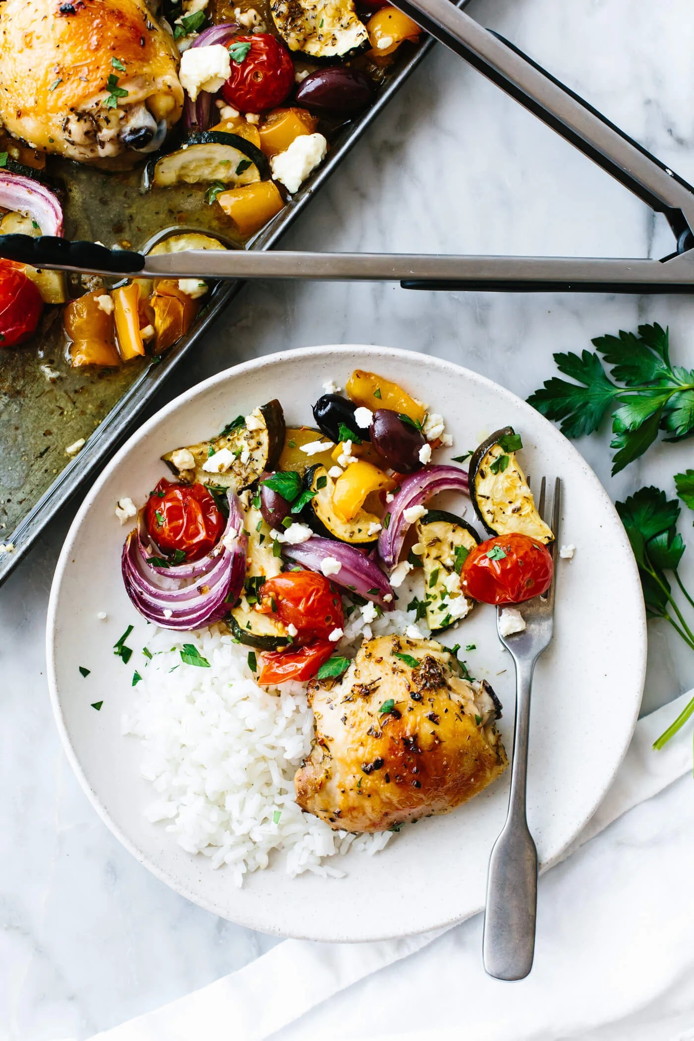 Greek sheet pan chicken plated with rice next to tongs.