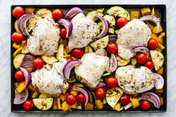 Greek chicken thighs with vegetables on a sheet pan.