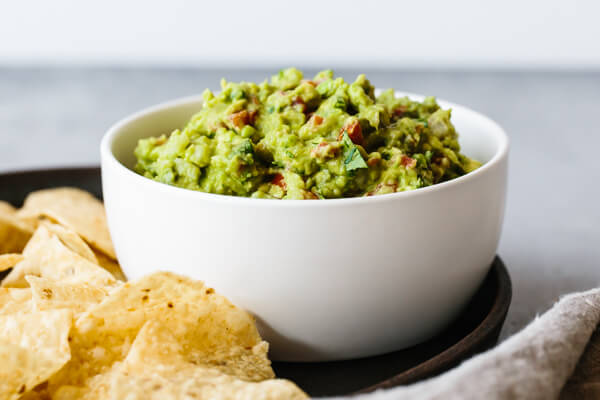 Guacamole in a serving bowl next to tortilla chips.