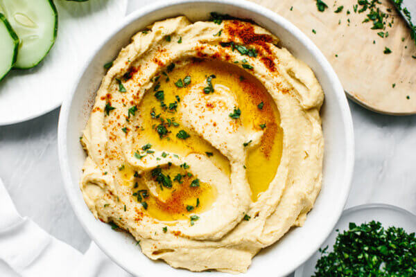 Hummus in a white bowl next to cucumbers
