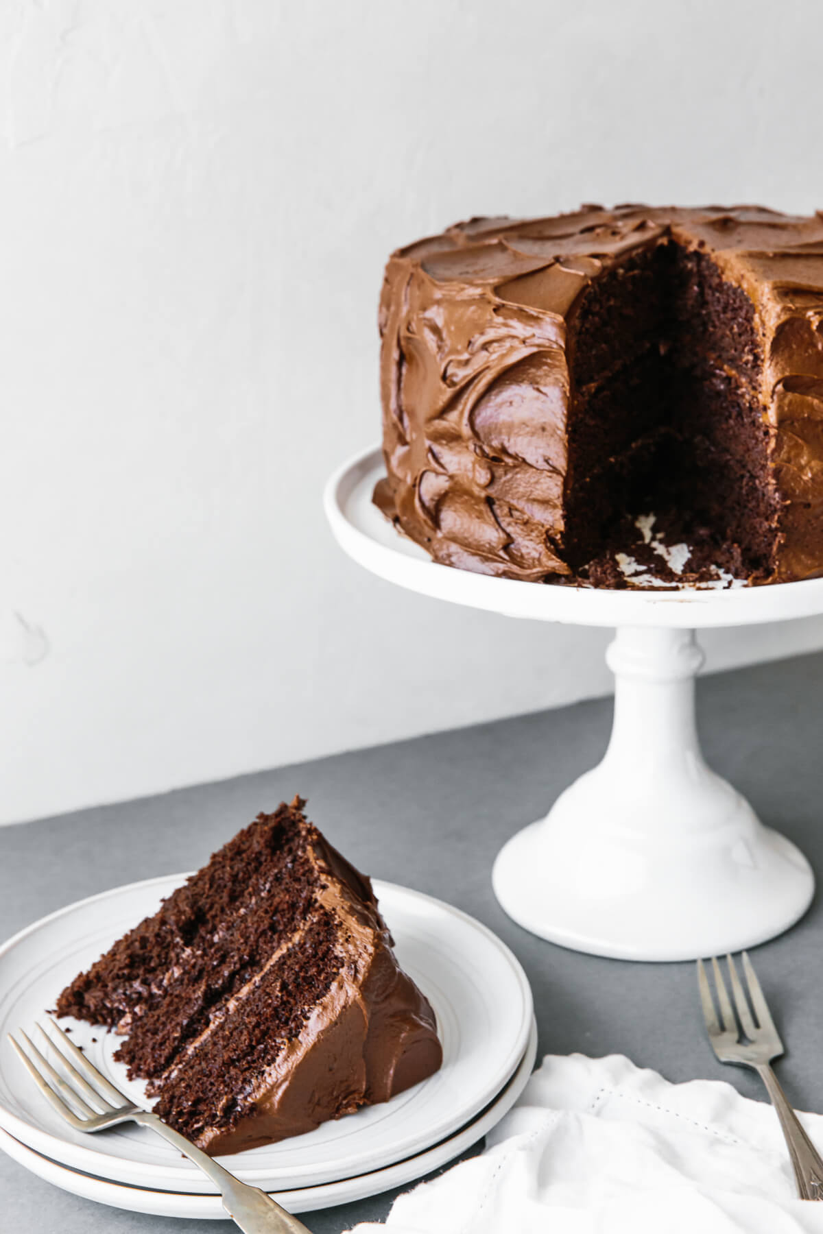 Paleo chocolate cake on a cake stand with slice removed to a plate.