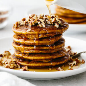 A stack of paleo pumpkin pancakes topped with pecans and maple ginger syrup.