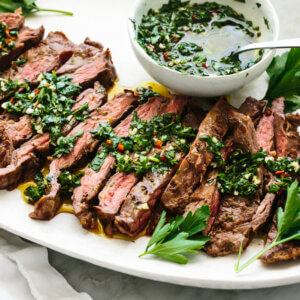 A large platter of skirt steak with chimichurri sauce