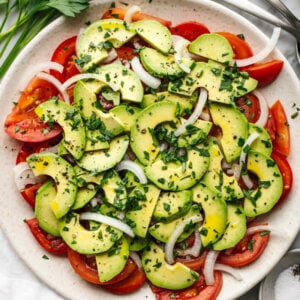A plate of tomato, onion, avocado salad on a table.