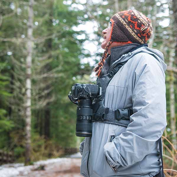 Man wearing a heavy duty hands-free camera harness holding his DSLR camera and lens while hiking