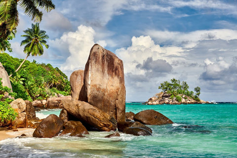 A breathtaking view of the Seychelles landscape, showcasing turquoise waters, white sandy beaches, lush greenery, granite boulders, and clear blue skies